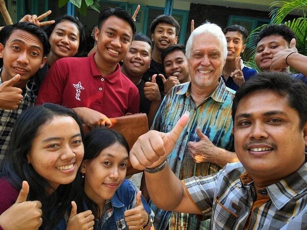A group of smiling Indonesian young people surround an older white man