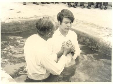 an older man baptizes a younger man in a pool of water