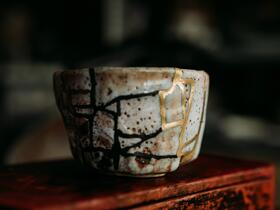 Kintsugi: a rough pottery cup with broken seams filled with gold